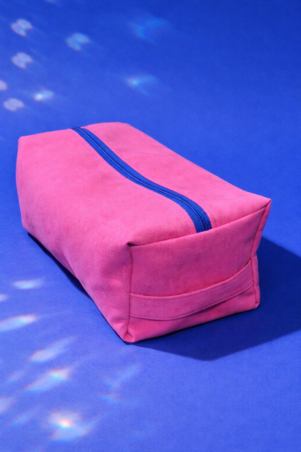 Pink toiletry bag with blue zipper on a blue background