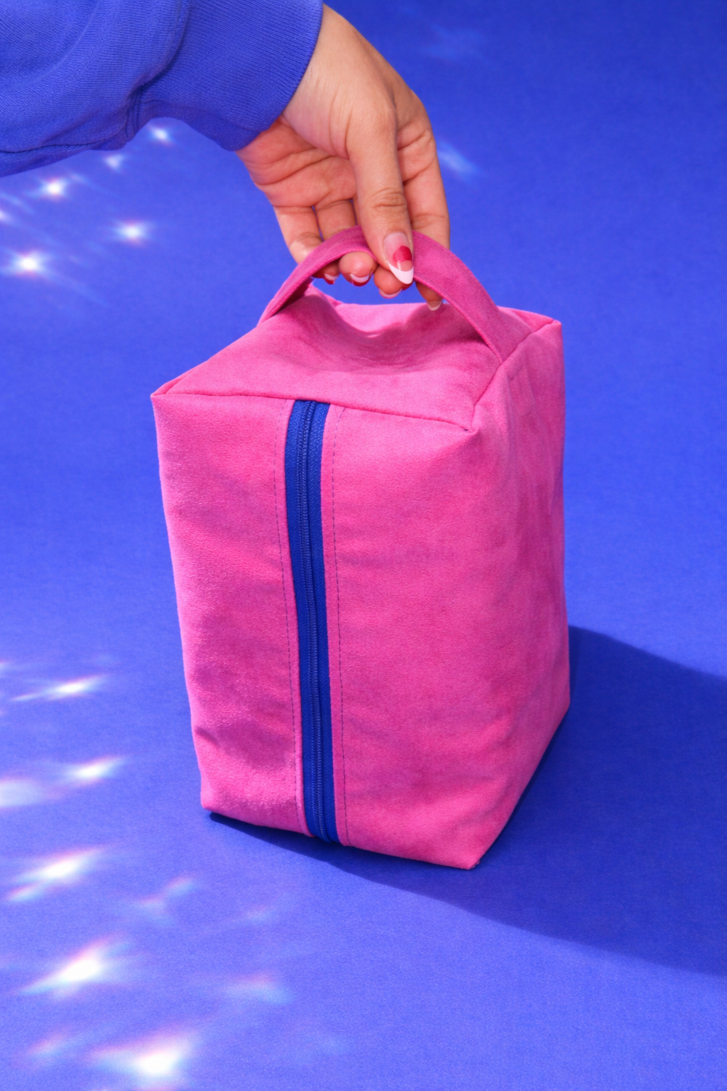 Pink bag with a blue zipper held by a hand against a blue background
